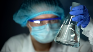 Laboratory technician in PPE reviewing water sample, for water risk management. 